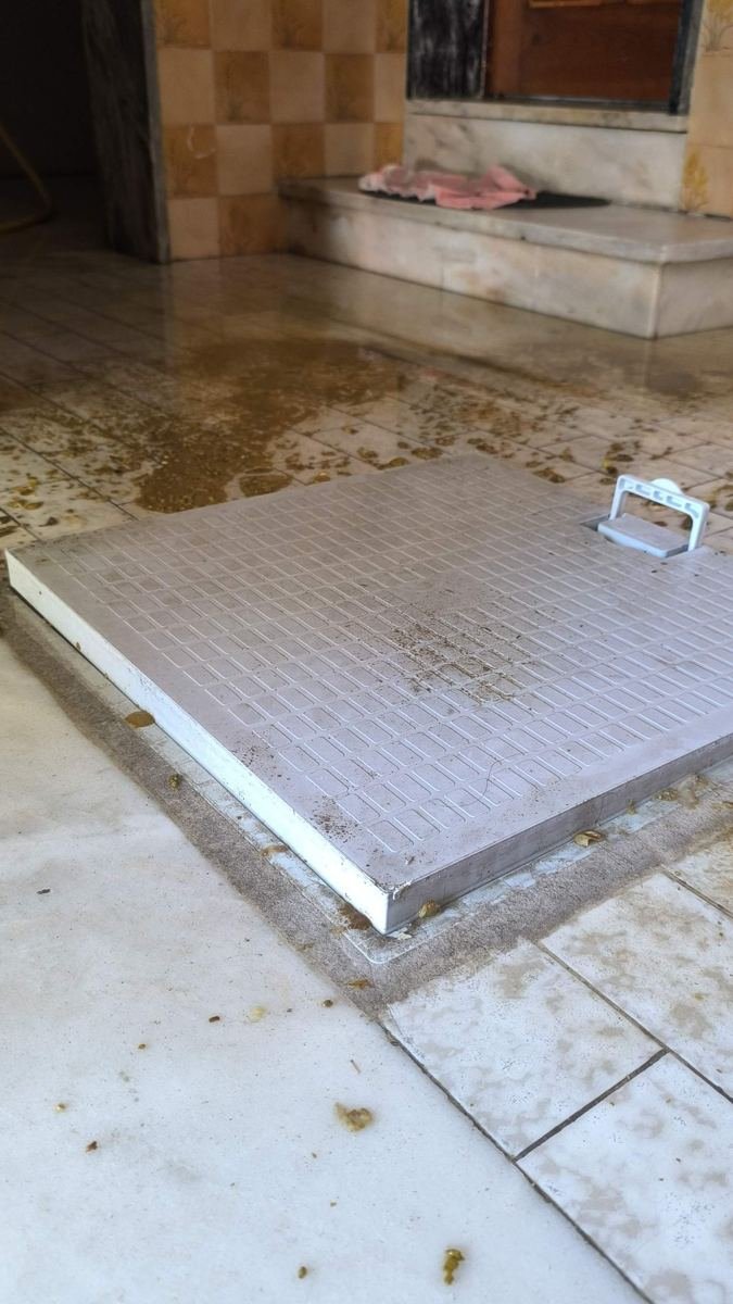 Tampa de caixa de esgoto levantada pela pressão, com água residual no piso